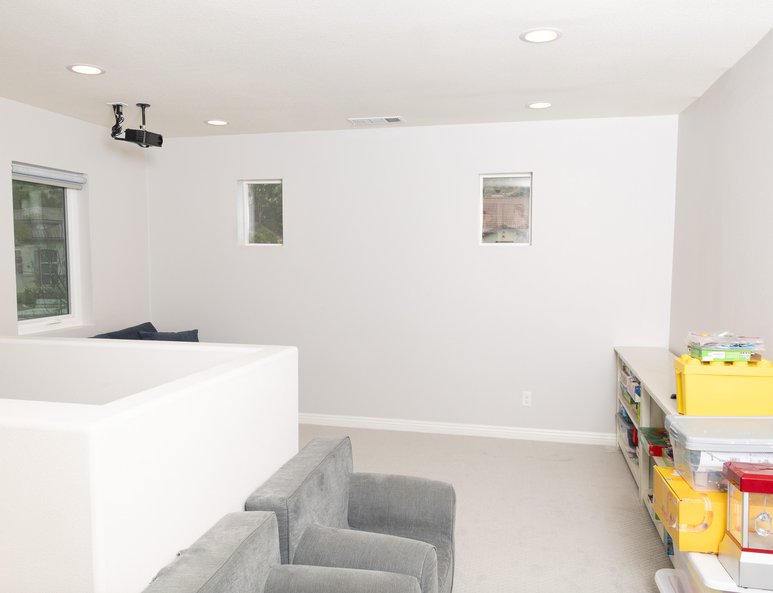 Loft play area after renovation with beige carpet, toy bins, white half wall, gray walls, and recessed lighting.
