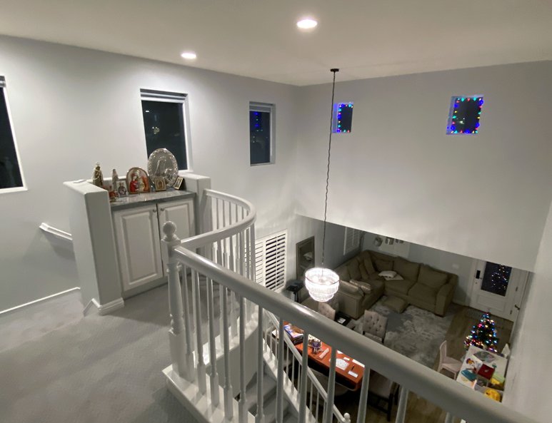 Upper landing before renovation with white railing, dark flooring, high ceiling, and open overlook into the living room below.