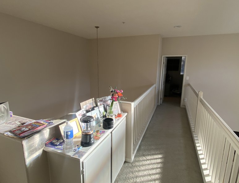 Upper hallway before renovation with beige carpet, white half wall, and natural light casting shadows across the walkway.