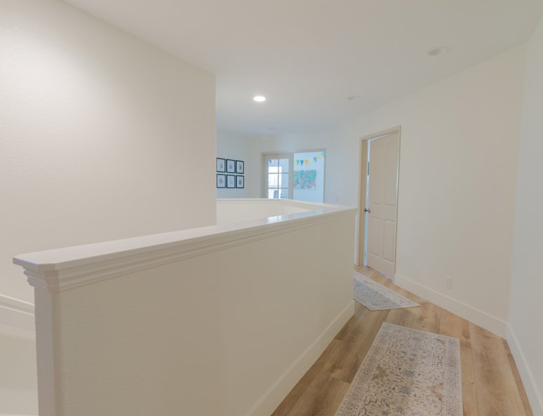 Upper landing after renovation with wood-look flooring, white half wall, neutral walls, and view toward adjoining rooms.