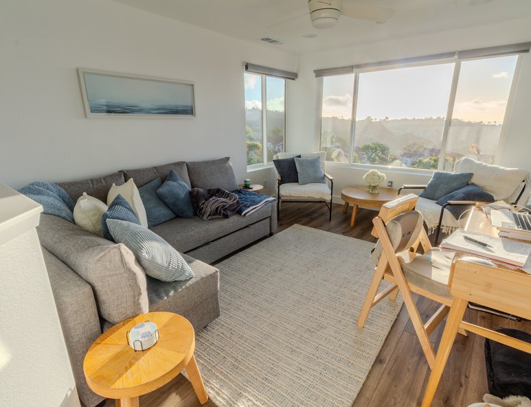 Sitting area after renovation with accent chairs, couch, small round table, large picture window, and scenic outdoor views.