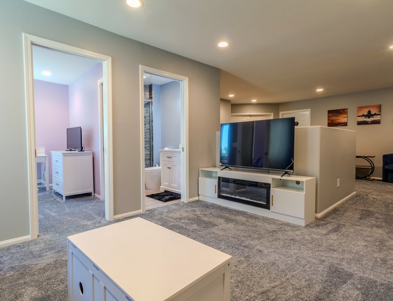 Open loft area after renovation with gray carpet, white entertainment console, recessed lighting, and access to multiple adjoining rooms.