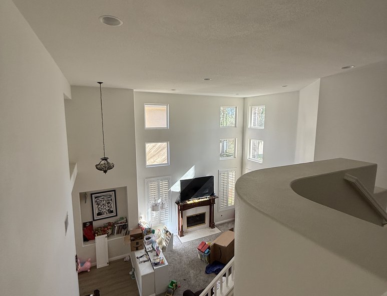 Two-story living room before renovation with staircase, tall walls, clerestory windows, gray carpet, and open overlook above.