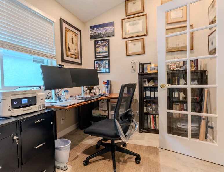 Home office after renovation with desk workspace, computer, bookcases, framed artwork, and French doors opening to an upper landing.