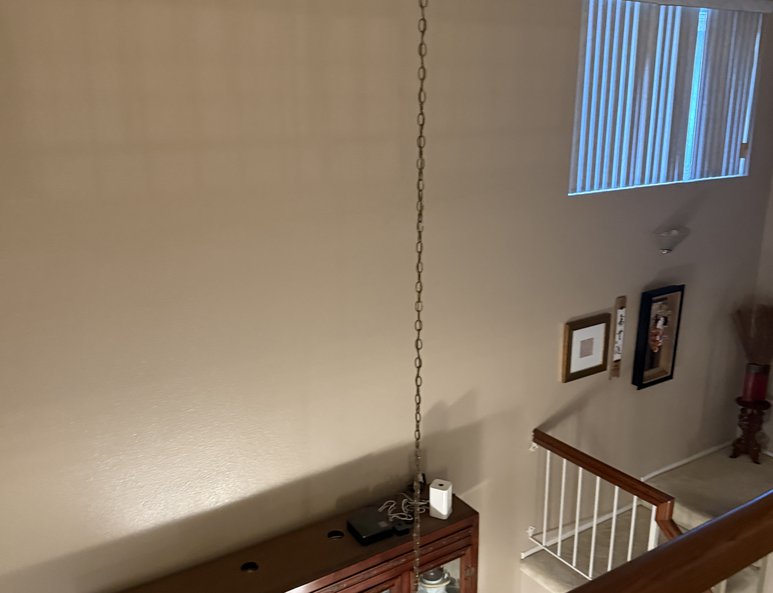 Upper landing before renovation with beige walls, wood railing, tall ceiling, and view downward into the foyer below.