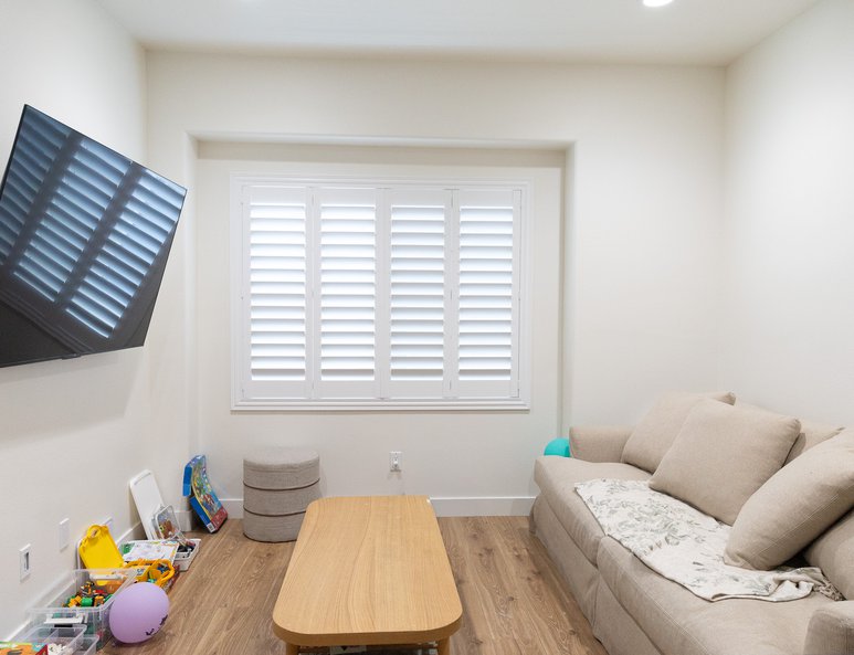 Loft family room after renovation with sectional sofa, wood-look flooring, large window with plantation shutters, and children's toys nearby.